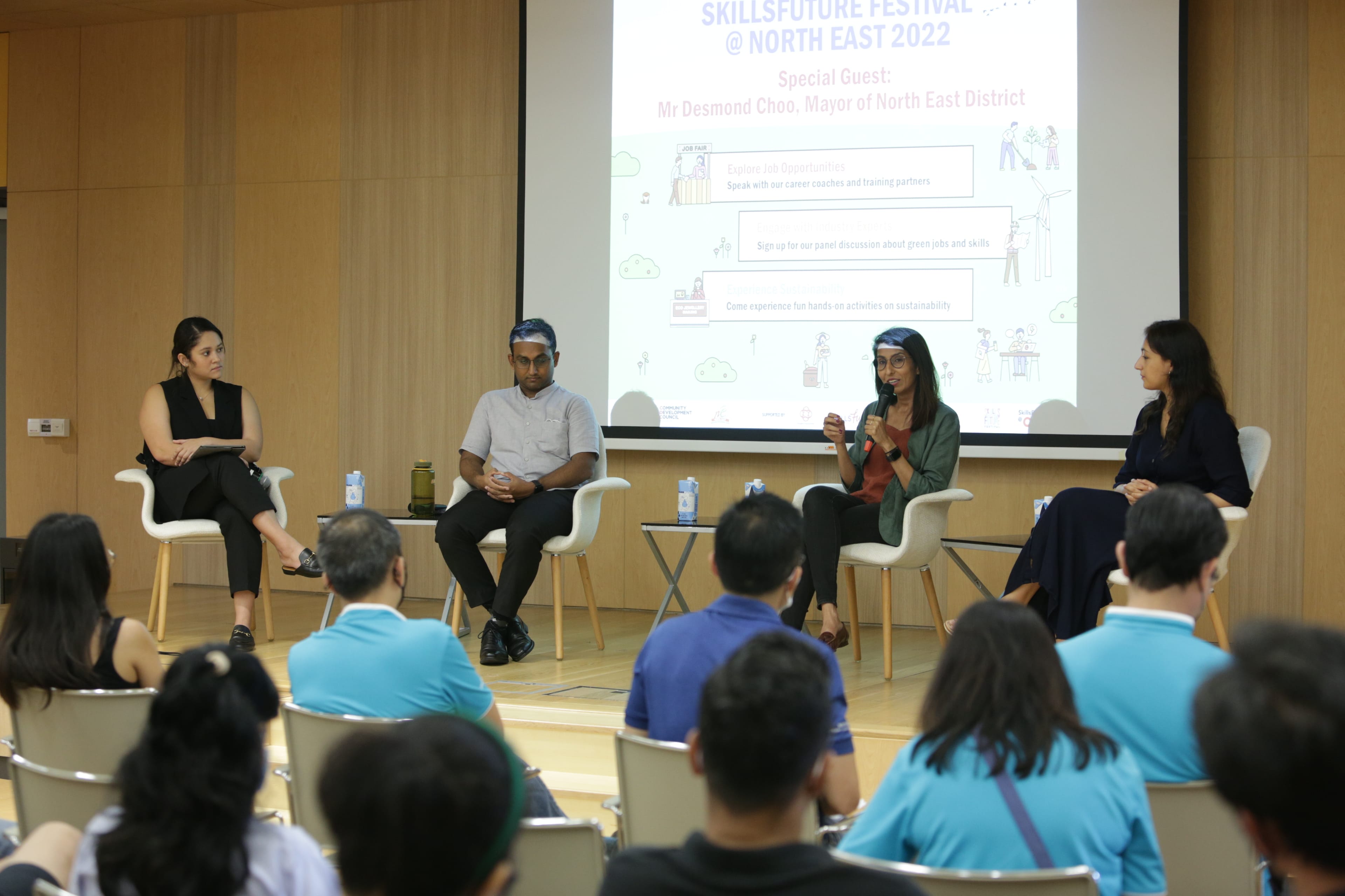 Four panelists are seated and facing an audience in a room with a SkillsFuture Festival sign on the wall.